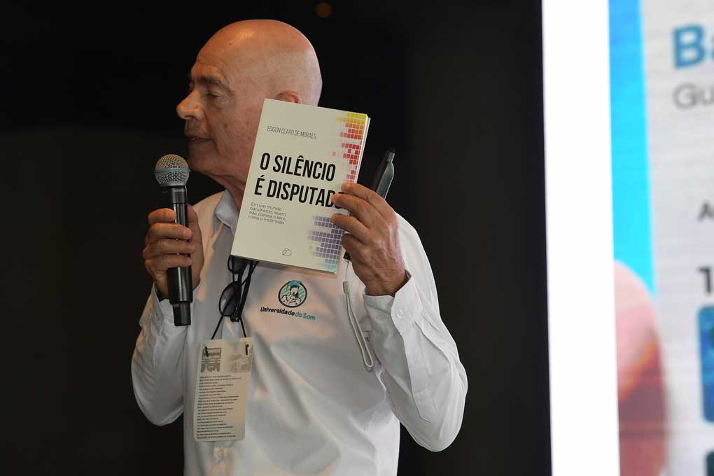 Diretor segurando um livro e apresentando o mesmo falando ao microfone num evento
