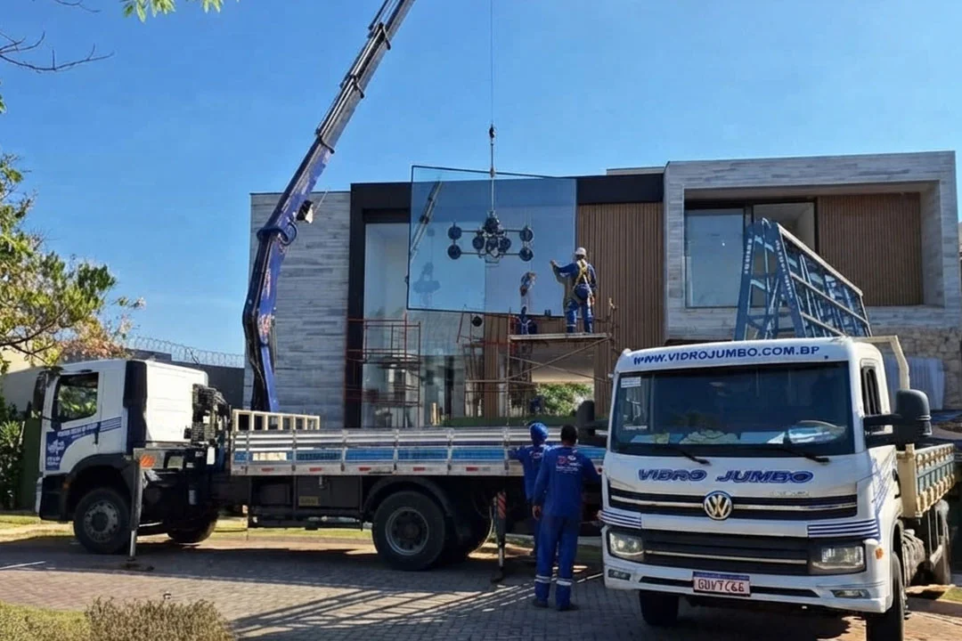 Caminhão munck da Vidro Jumbo realizando o içamento de vidro de grandes dimensões em fachada de casa de alto padrão em São Paulo. Operação técnica com equipamento de ventosa de alta segurança e equipe especializada.