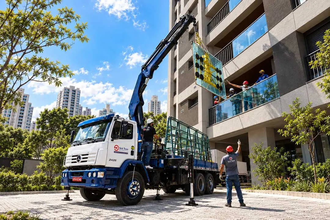 Equipe da Tech Trans realiza transporte e içamento profissional de painel de vidro em edifício, utilizando caminhão munck e equipamento especializado.